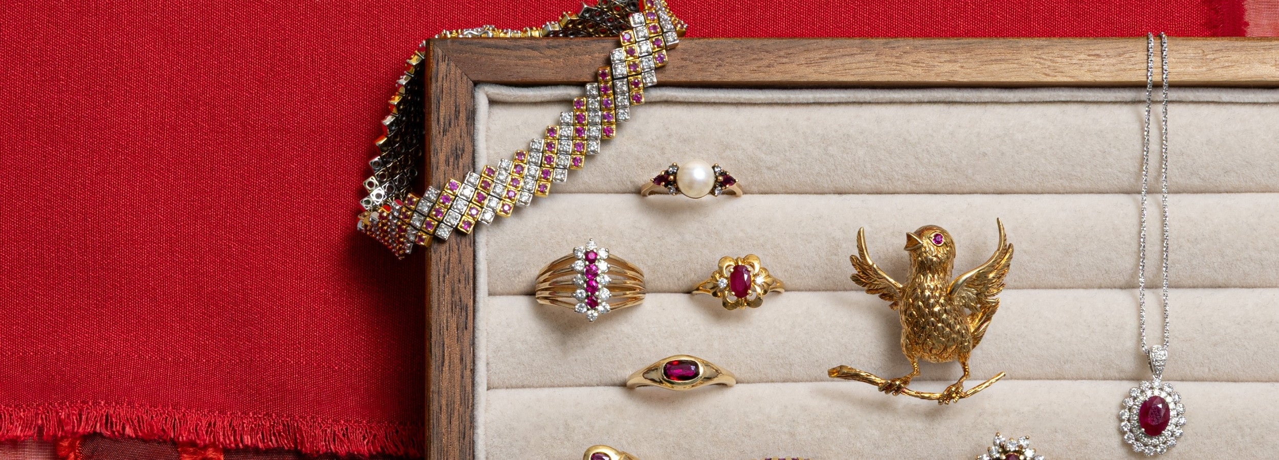 Curated collection of vintage ruby rings, a fine jewellery gold bird brooch, and a diamond bracelet in a velvet jewelry tray.