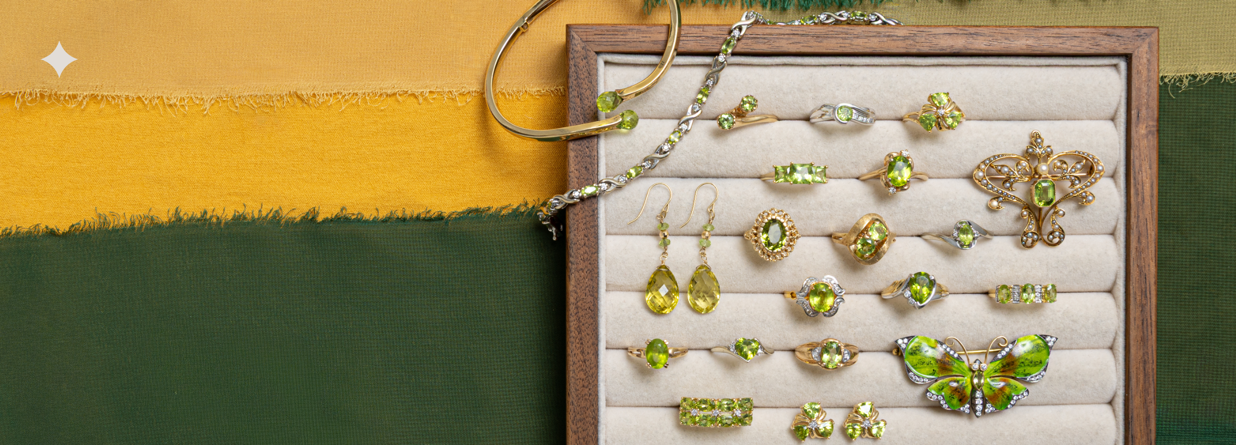 A jewelry display board filled with multiple rings, earrings, and a bracelet, each featuring green peridot gemstones in yellow gold and white gold settings, set against a split yellow and dark green background.