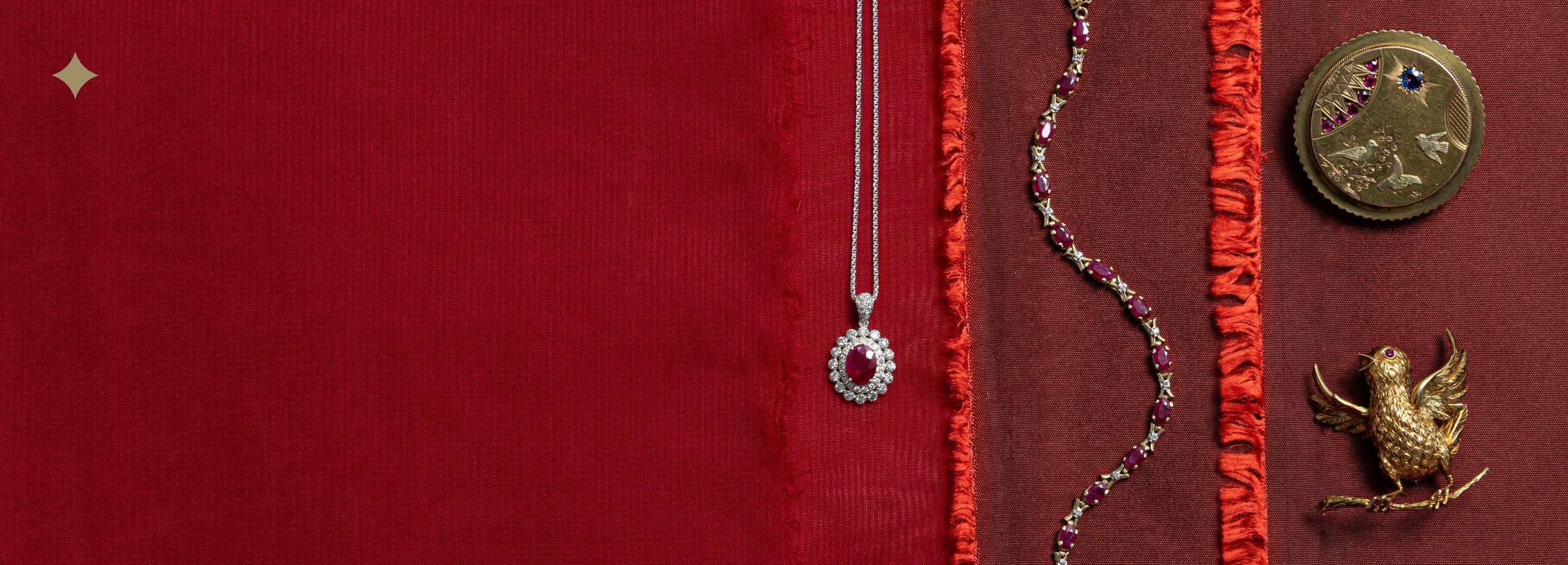 Collection of preloved fine jewelry for the July birthstone, featuring a vintage ruby halo pendant necklace, x cross style ruby tennis bracelet, an engraved textured brooch, and an antique bird brooch on textured red fabric.