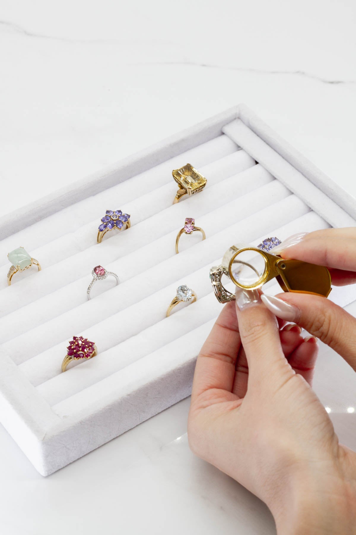 image of woman inspecting vintage jewelry with a loop magnifying glass. selection of gemstone rings in velvet tray