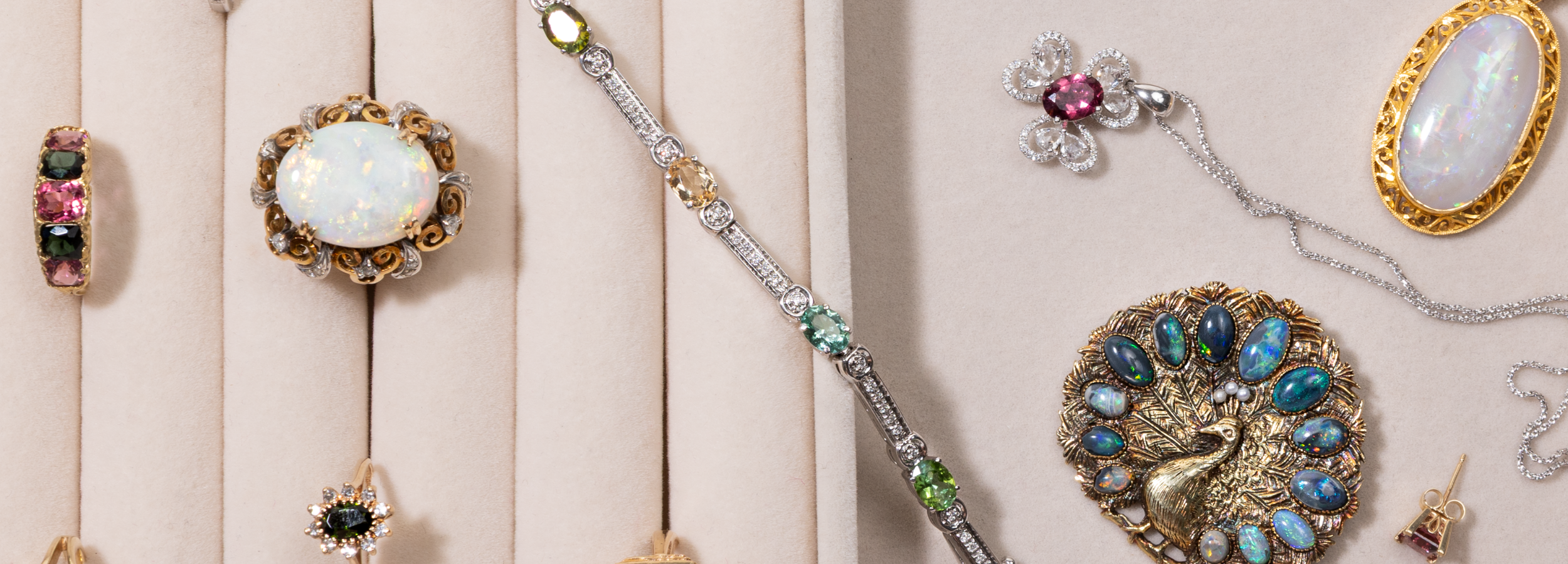 Collection of decorative, vintage brooches, bracelets, rings, pendants with opals, diamonds, and tourmaline gemstones on a beige background and tray. 