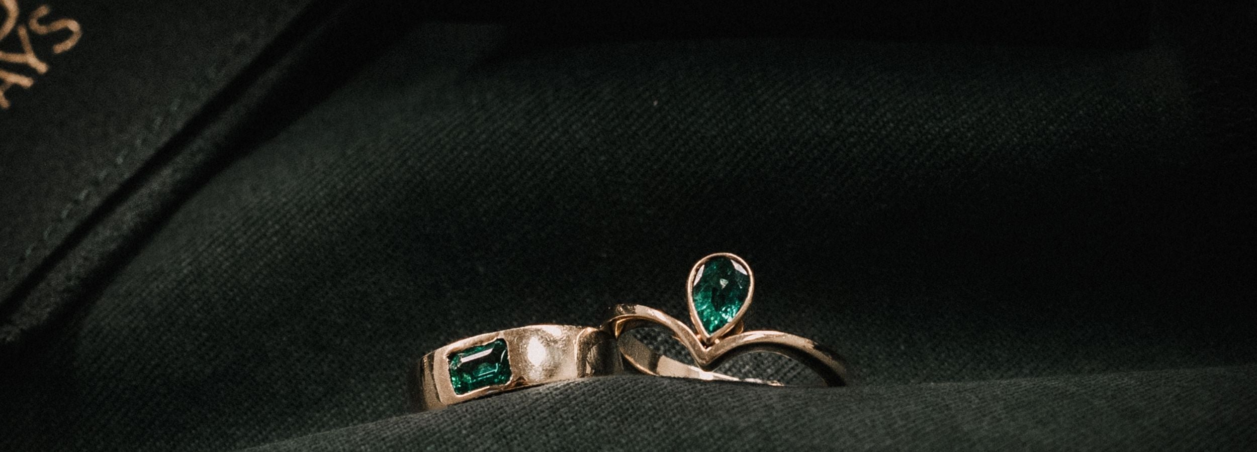 Minimalist fine jewelry stack featuring a teardrop emerald ring and a gold band with a rectangular, east to west emerald.