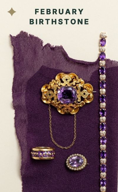 Ornate antique gold brooch with a large oval amethyst gemstone styled on textured purple fabric, part of a February birthstone jewellery edit.