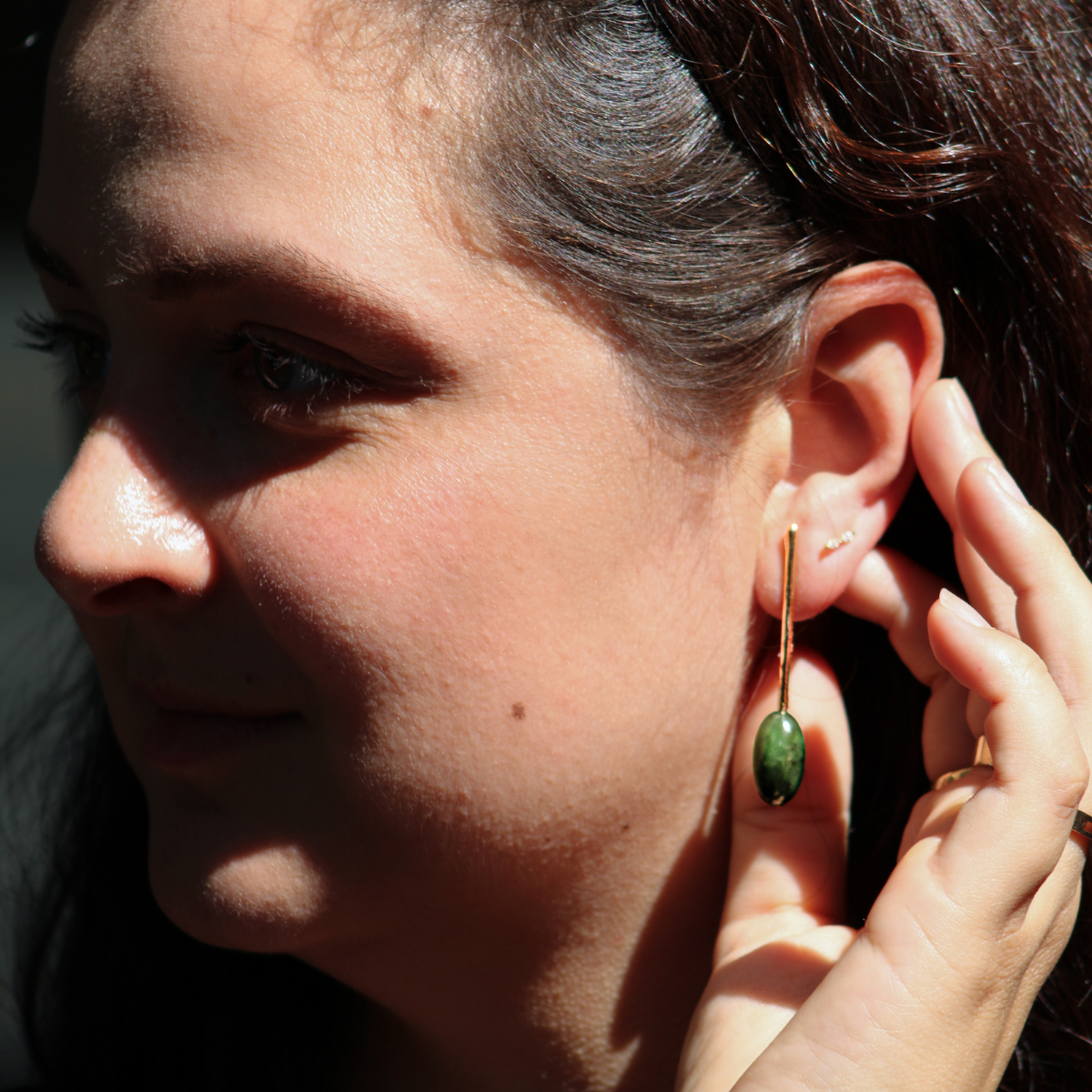 Close-up of a woman in sunlight wearing a unique vintage nephrite jade drop earrings, highlighting elegant preloved statement jewelry.