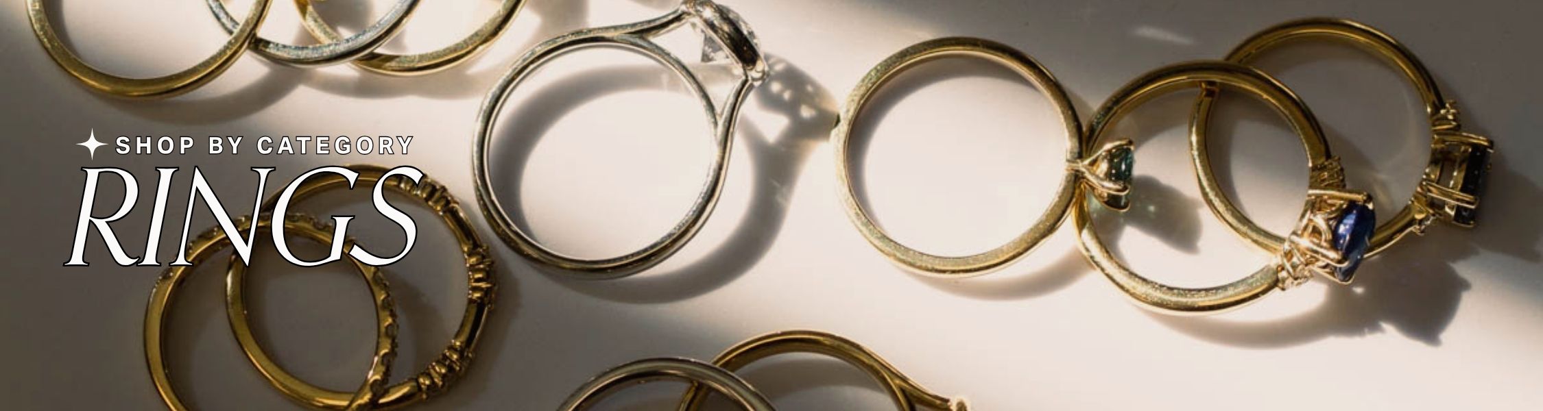 Yellow and White Gold rings with gemstones on a light background, text reads: 'Shop by Category: Rings'.