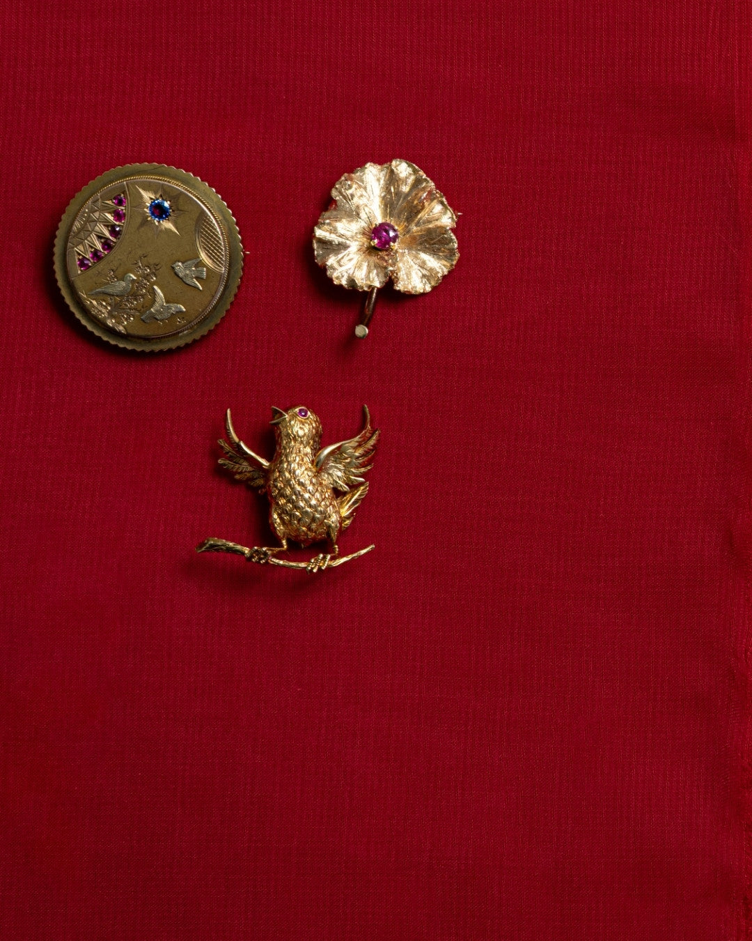 Flat lay of timeless heirloom pieces and preloved fine jewelry, featuring a natural ruby floral pendant, a textured gold vintage brooch, and a vintage gold bird pin.
