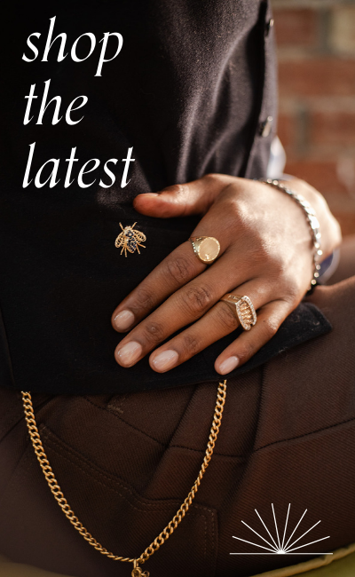 Hand wearing vintage gold, signet rings and antique watch chain styled with tailored outfit and bee brooch. Text reads: shop the latest