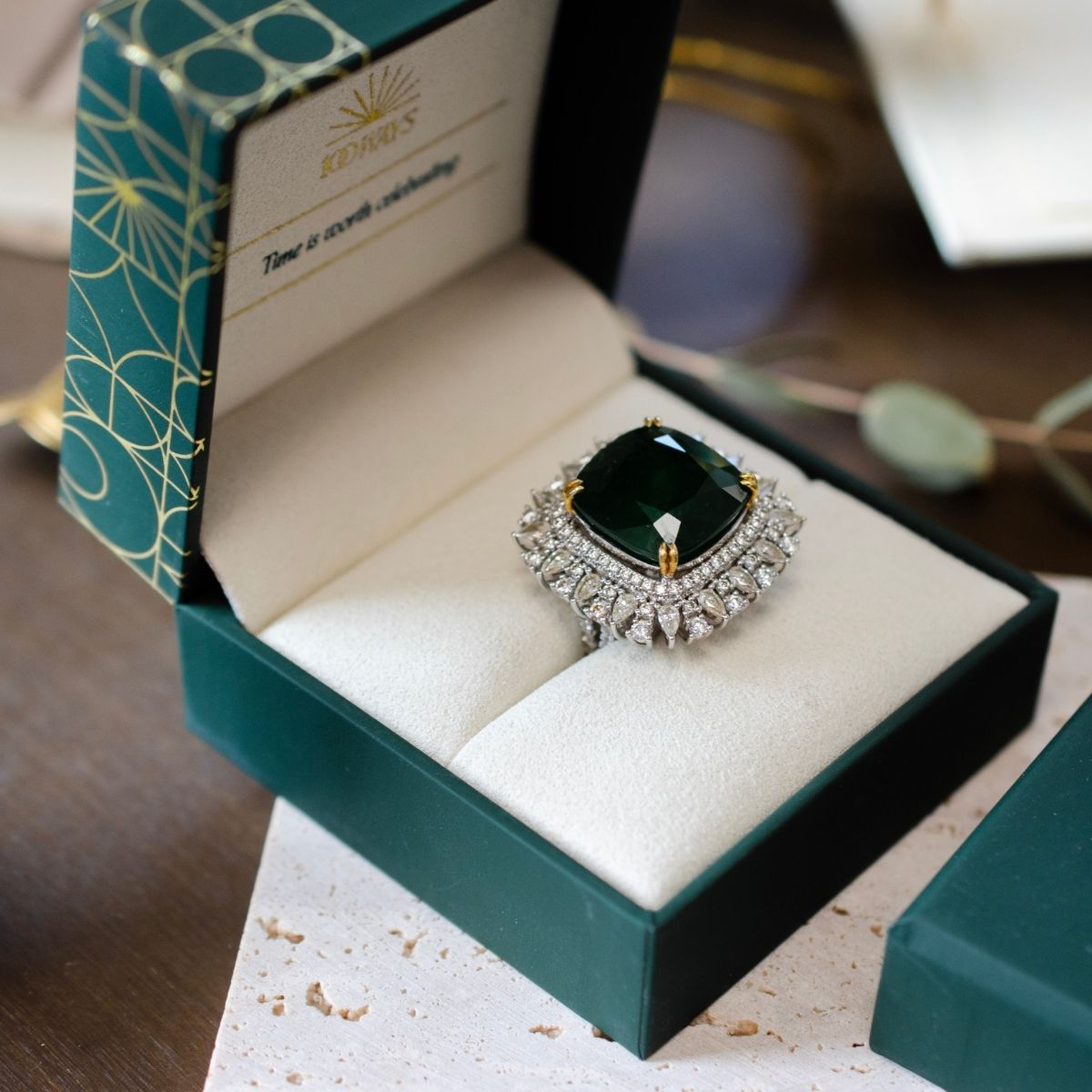 Luxurious large emerald cocktail ring with diamond halo in a green velvet jewelry gift box.
