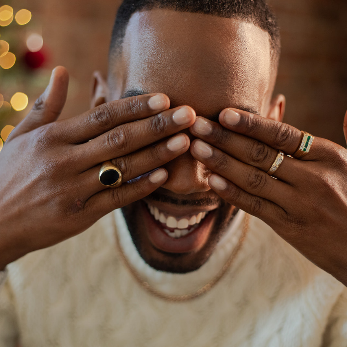 Man laughing with hands over eyes, wearing oval onyx ring, vintage star set yellow gold band and emerald and diamond accent ring. 