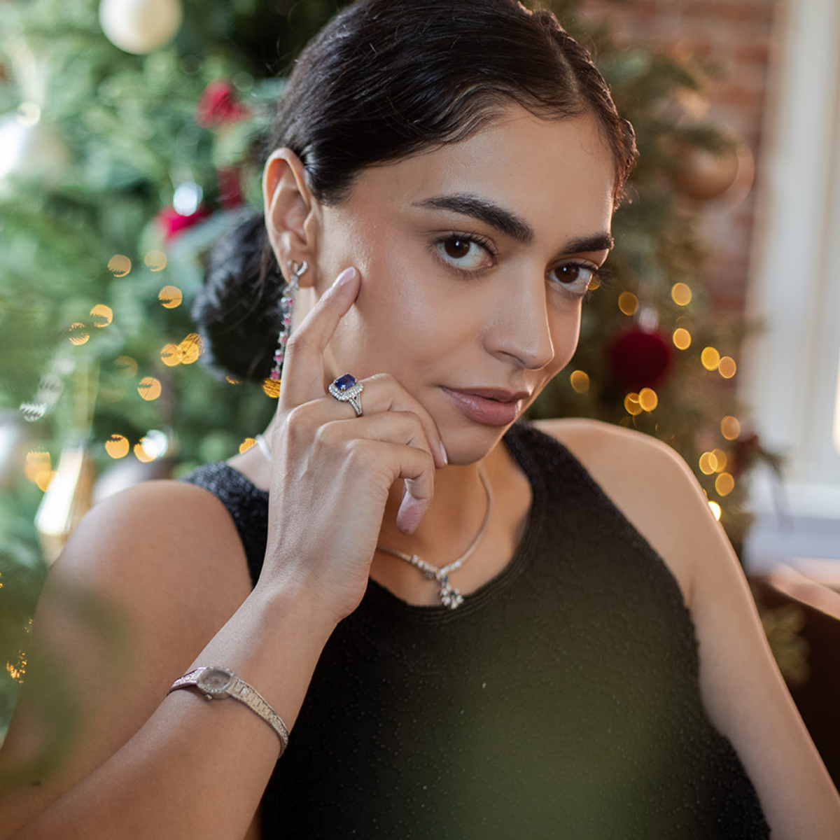 Woman posing by a Christmas tree, wearing vintage, antique white gold jewellery adorned with ruby, sapphire and diamonds. 