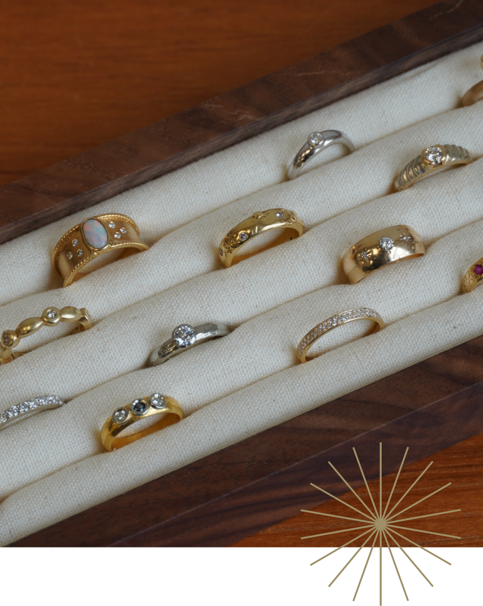 A collection of yellow gold and white gold rings displayed on a cream fabric-lined walnut jewelry tray, set against a dark wood background.