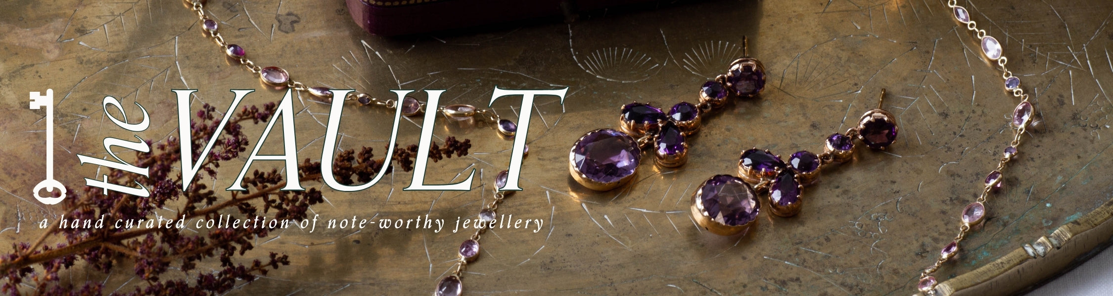 unique amethyst drop earrings and bezel set necklace on gold jewellery tray with dried florals. Overlay of 'The Vault' branding  and a key graphic. subtitle text reads: a hand curated collection of note-worthy jewellery