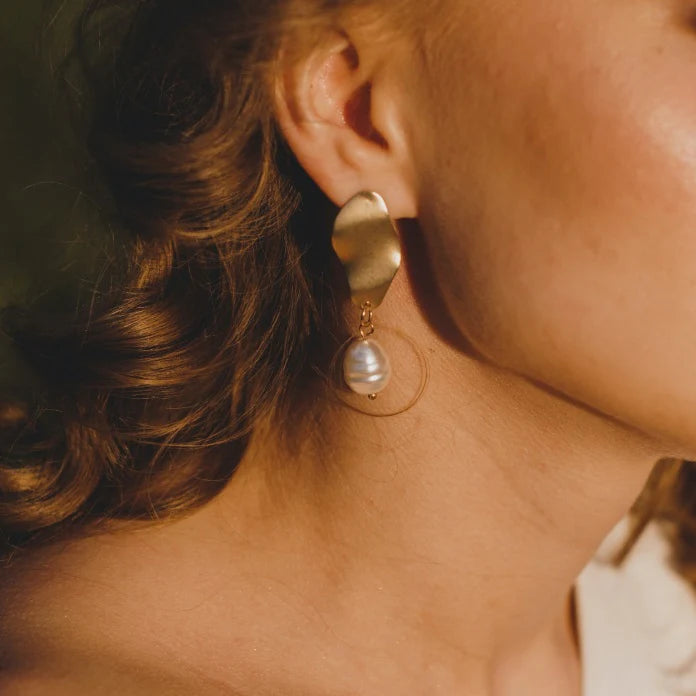 close up image of woman in golden light wearing gold and cultured pearl drop earrings