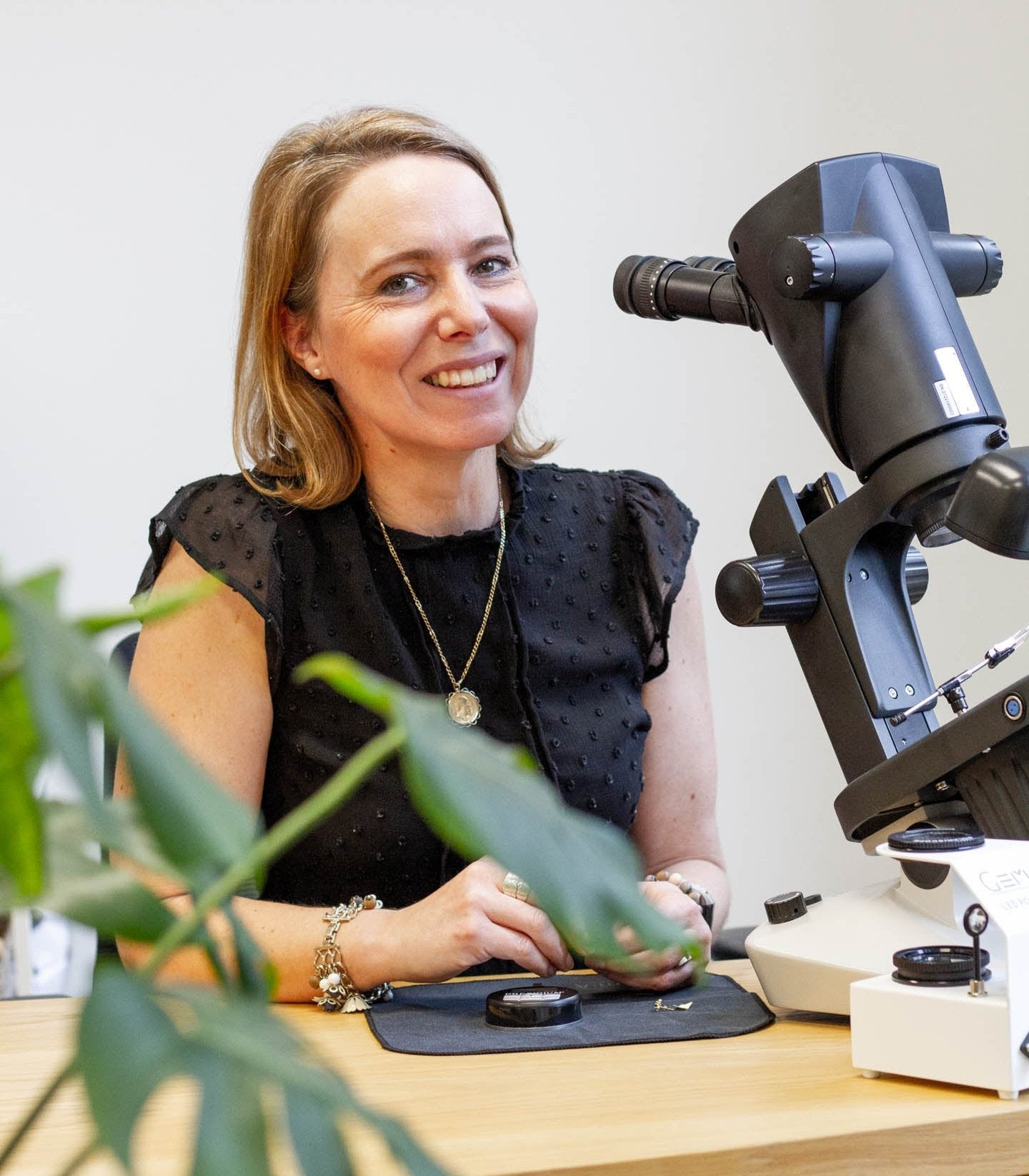 One of our 100 Ways gemologists smiling behind a microscope, working on jewelry authentication