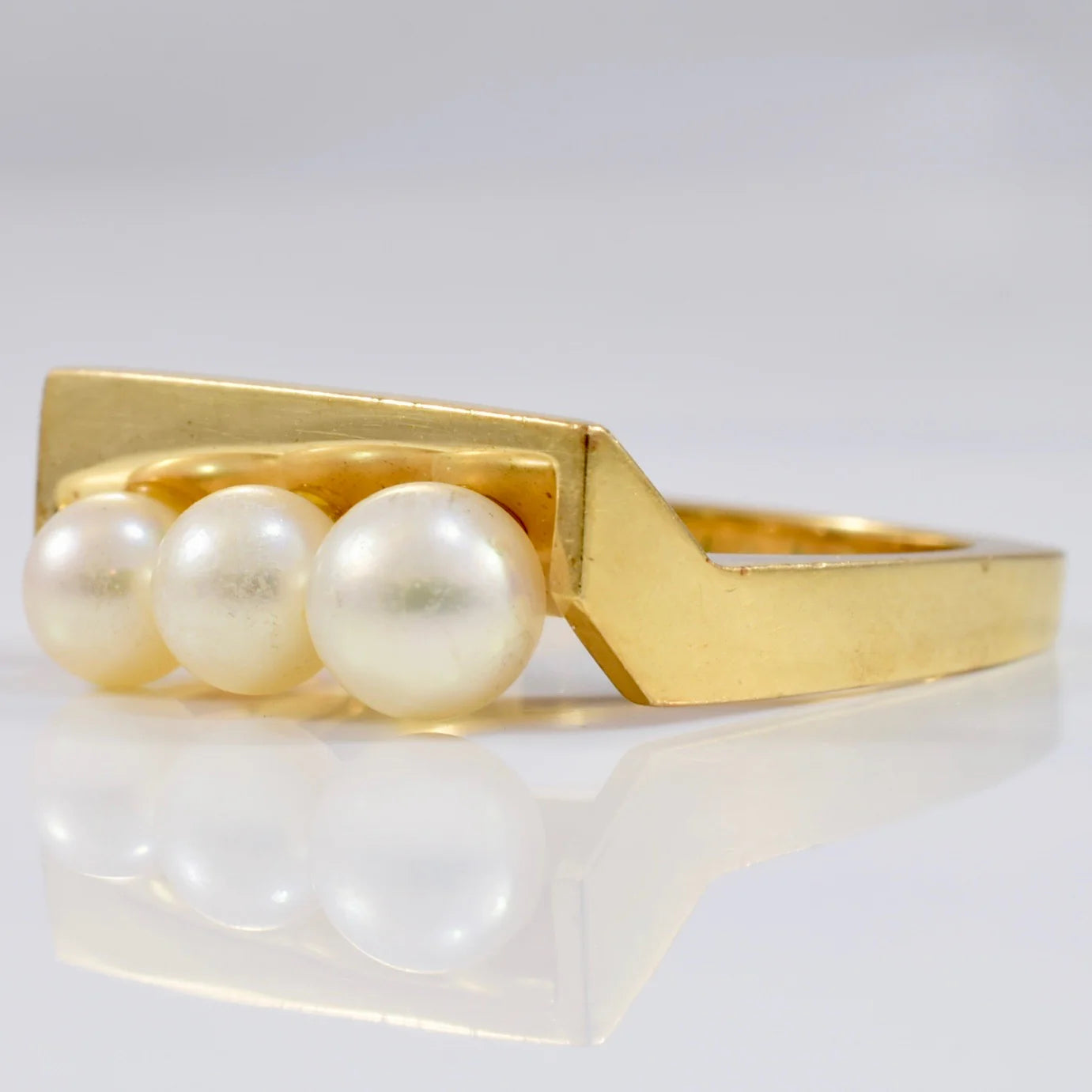 close up product shot of a yellow gold ring with three pearls, modern setting