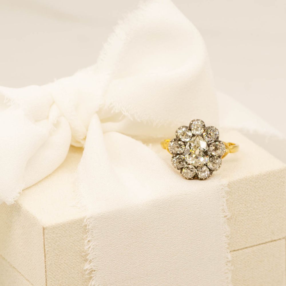 image of vintage pear cut and old mine cut diamonds set in a halo engagement ring on top of a beautiful ring box on creamy background