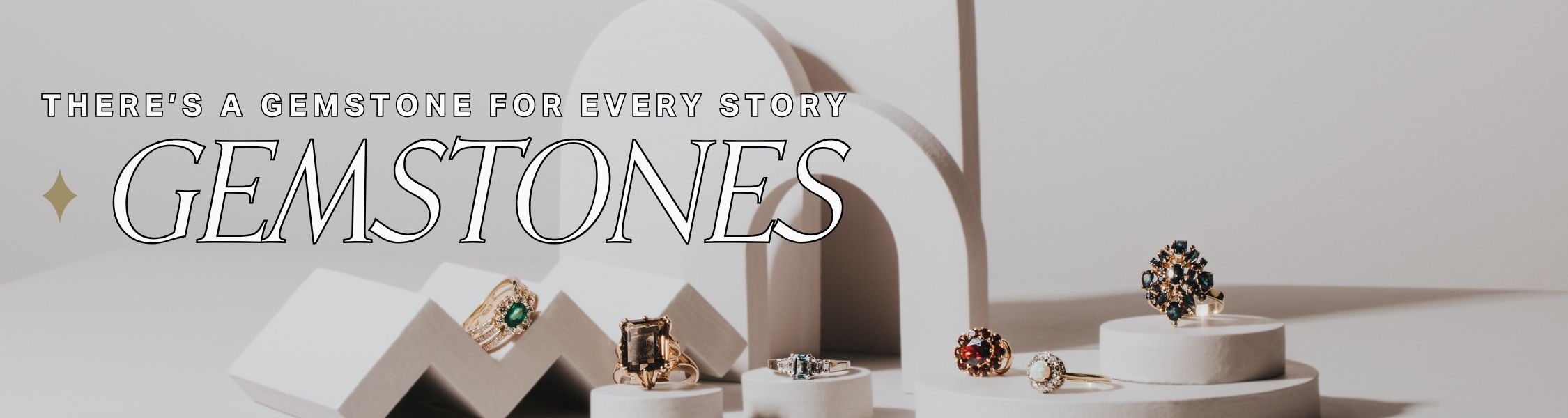 Jewelry display with gemstone rings on a white background, featuring the text 'There's a gemstone for every story'.