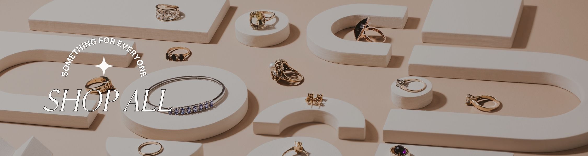 Jewelry display with rings and bracelets on a beige background, featuring a 'Shop All' call to action and text 'something for everyone'.