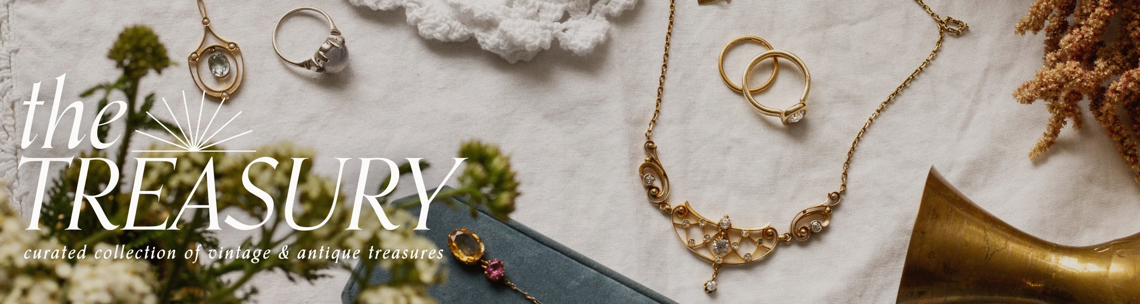 selection of vintage and antique Jewelry including rings and a necklace displayed on a textured fabric surface with vintage styling objects. Text overlay reads: The treasury: curated collection of vintage and antique treasures